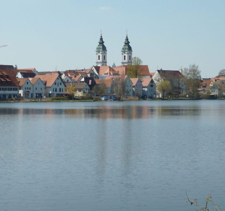 Stadtansicht mit Wasserreflexionen und zwei markanten Kirchtürmen.