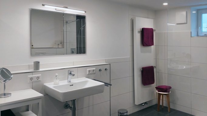 Heller Badezimmer mit Waschbecken, Spiegel, Handtüchern und Hocker.