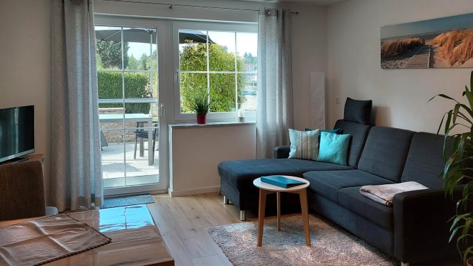 Helles Wohnzimmer mit Sofa, Tisch und Zugang zur Terrasse durch große Fenster.